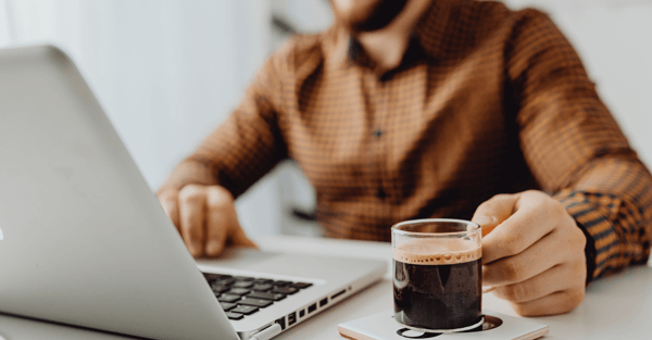 Image of a man working at a laptop with a cup of coffee.